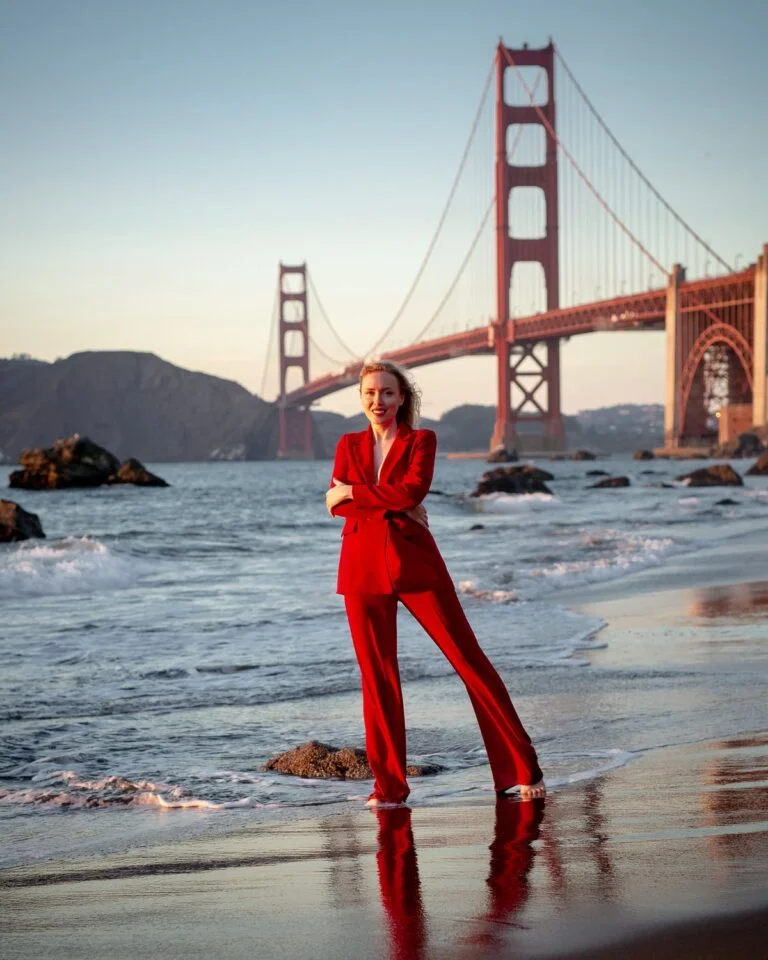 a person in a red dress standing in the water in front of a red bridge
