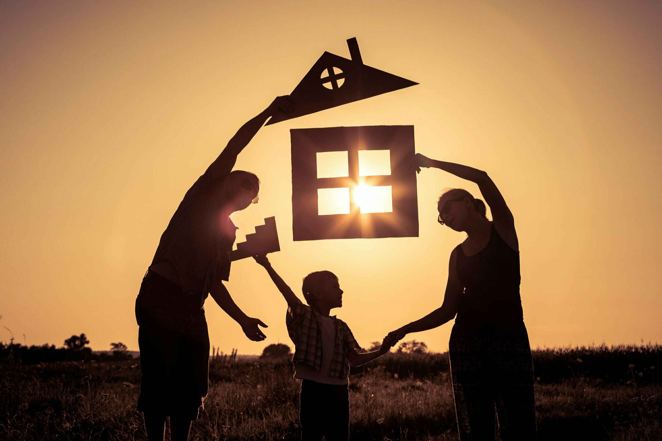 Happy family standing on the field at the sunset time. They build a house.