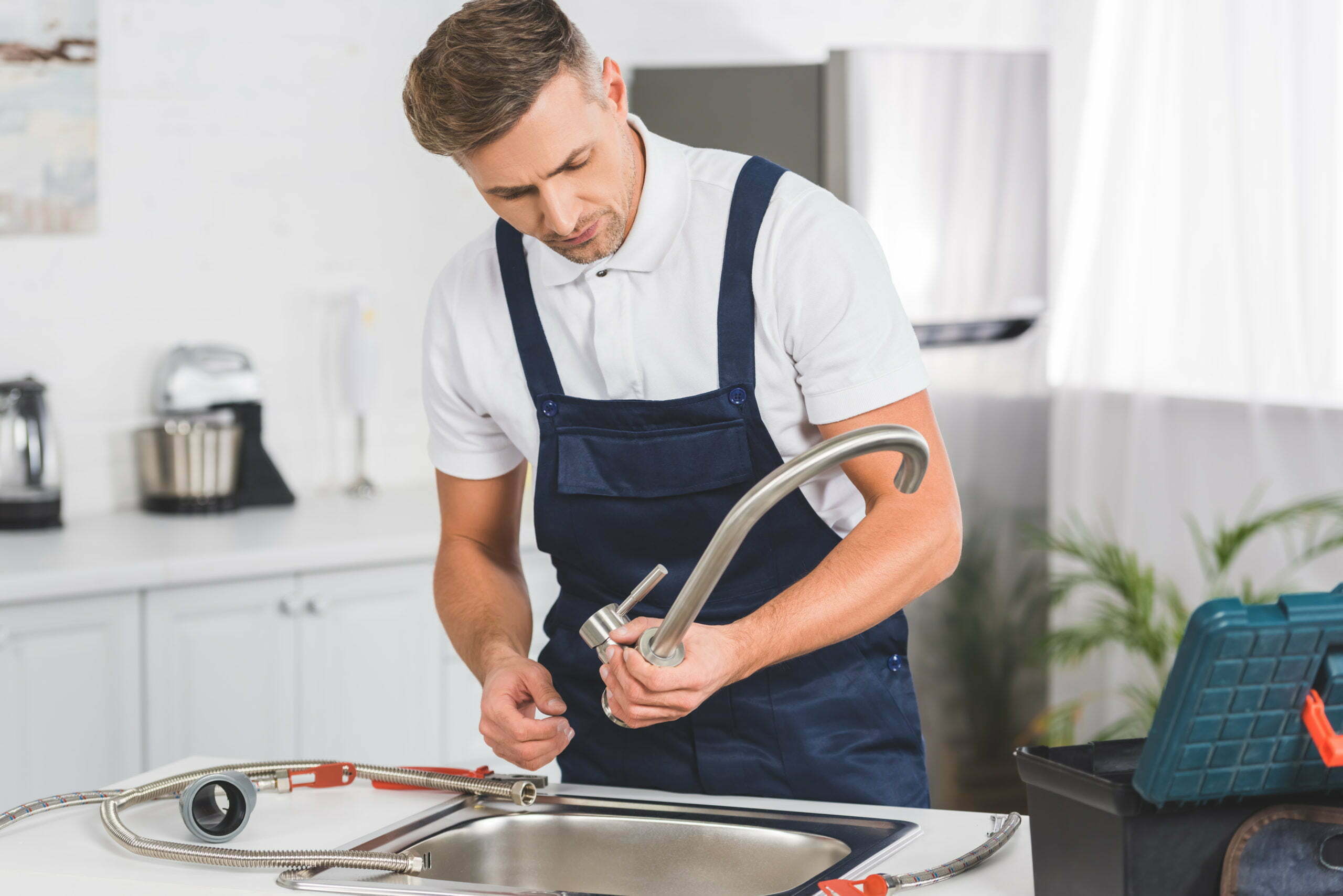 thoughtful adult repairman taking off kitchen faucet for repairing